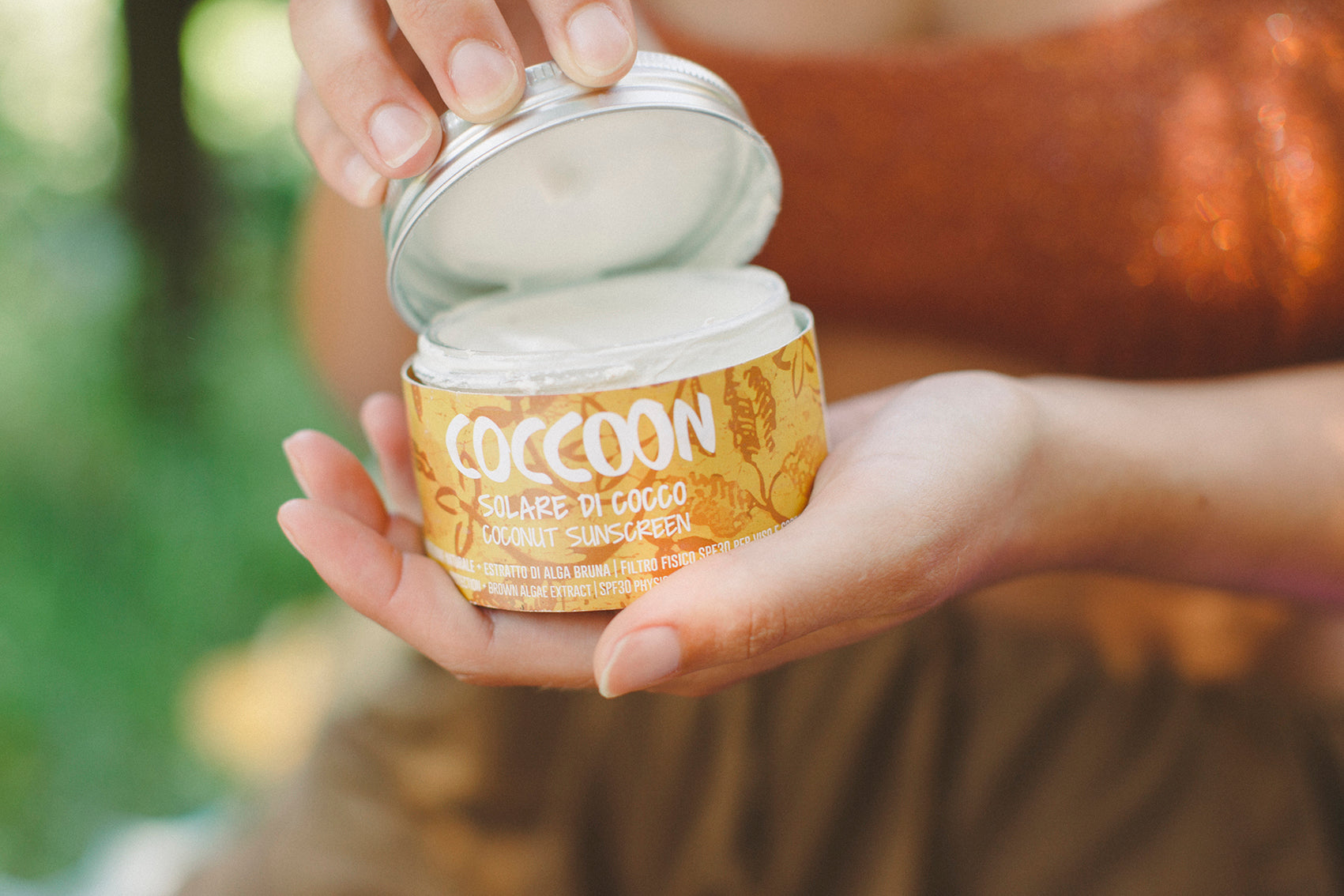 Una confezione di solare ecologico Coccoon tra le mani di una persona che lo sta aprendo per applicarlo sulla pelle.